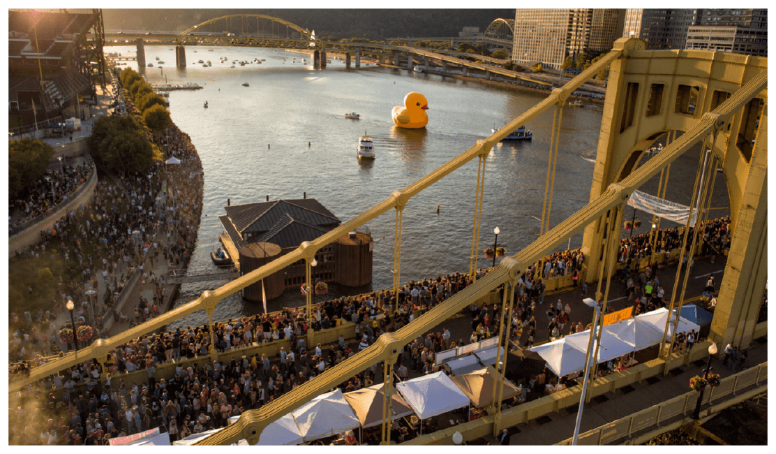 40-foot yellow rubber duck floating in Pittsburgh harbor with the city skyline behind it